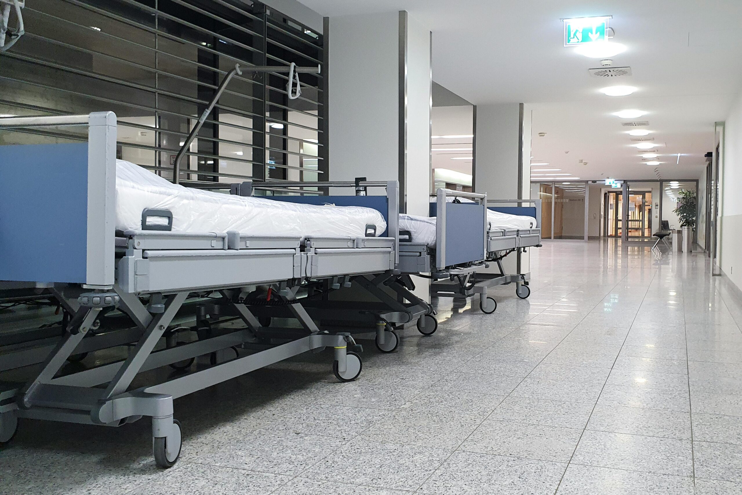 Quiet hospital hallway with neatly arranged empty medical beds under bright ceiling lights.